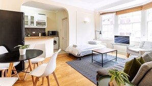 A modern apartment with a dining area, kitchen, living room, and a large window with a view. - Modern Flat Near Hyde Park (London)
