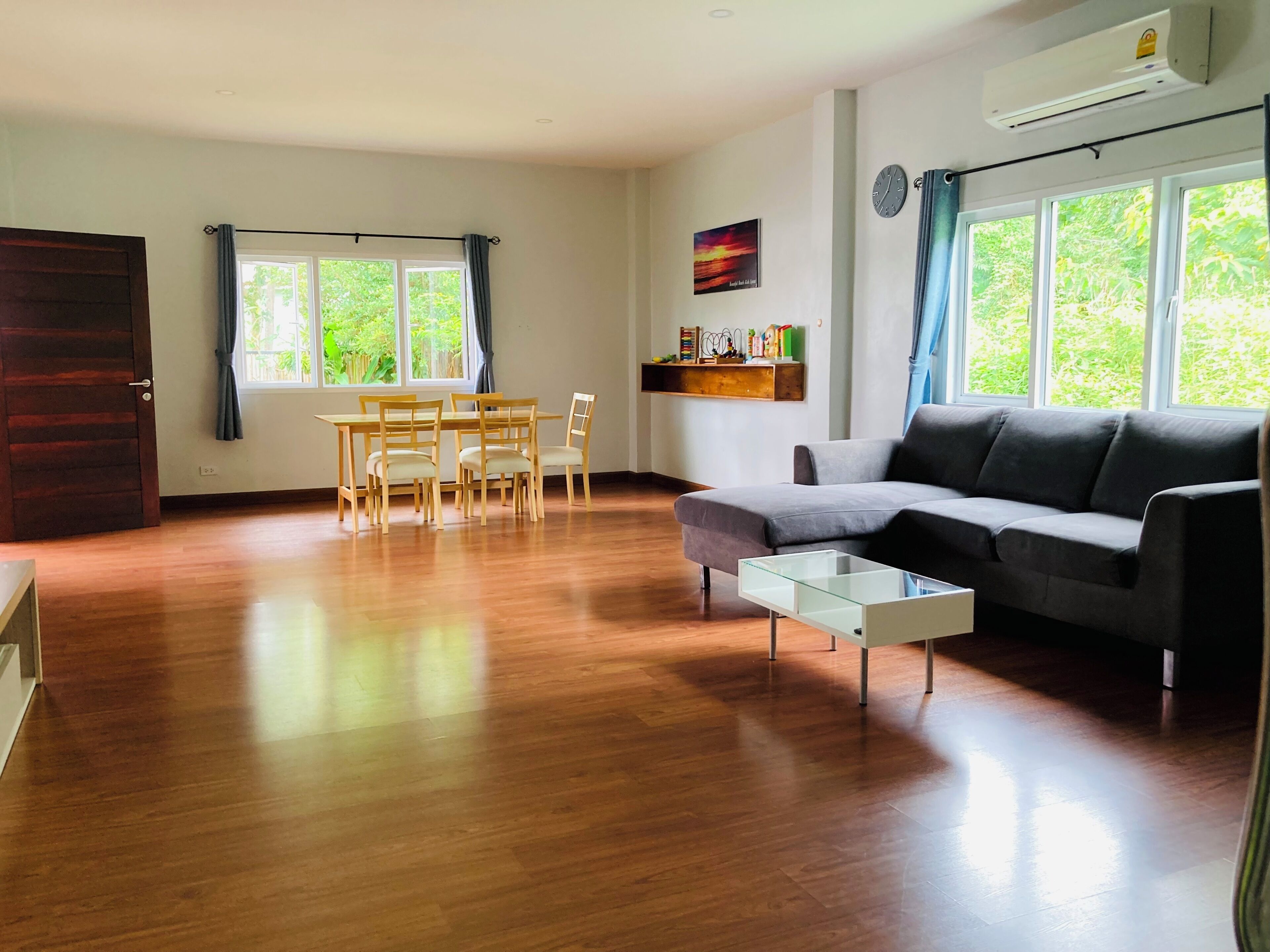 Un salon comprenant un canapé, une table basse en verre, des chaises en bois, une table à manger et une fenêtre avec des rideaux.