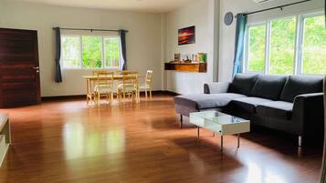 Un salon comprenant un canapé, une table basse en verre, des chaises en bois, une table à manger et une fenêtre avec des rideaux.