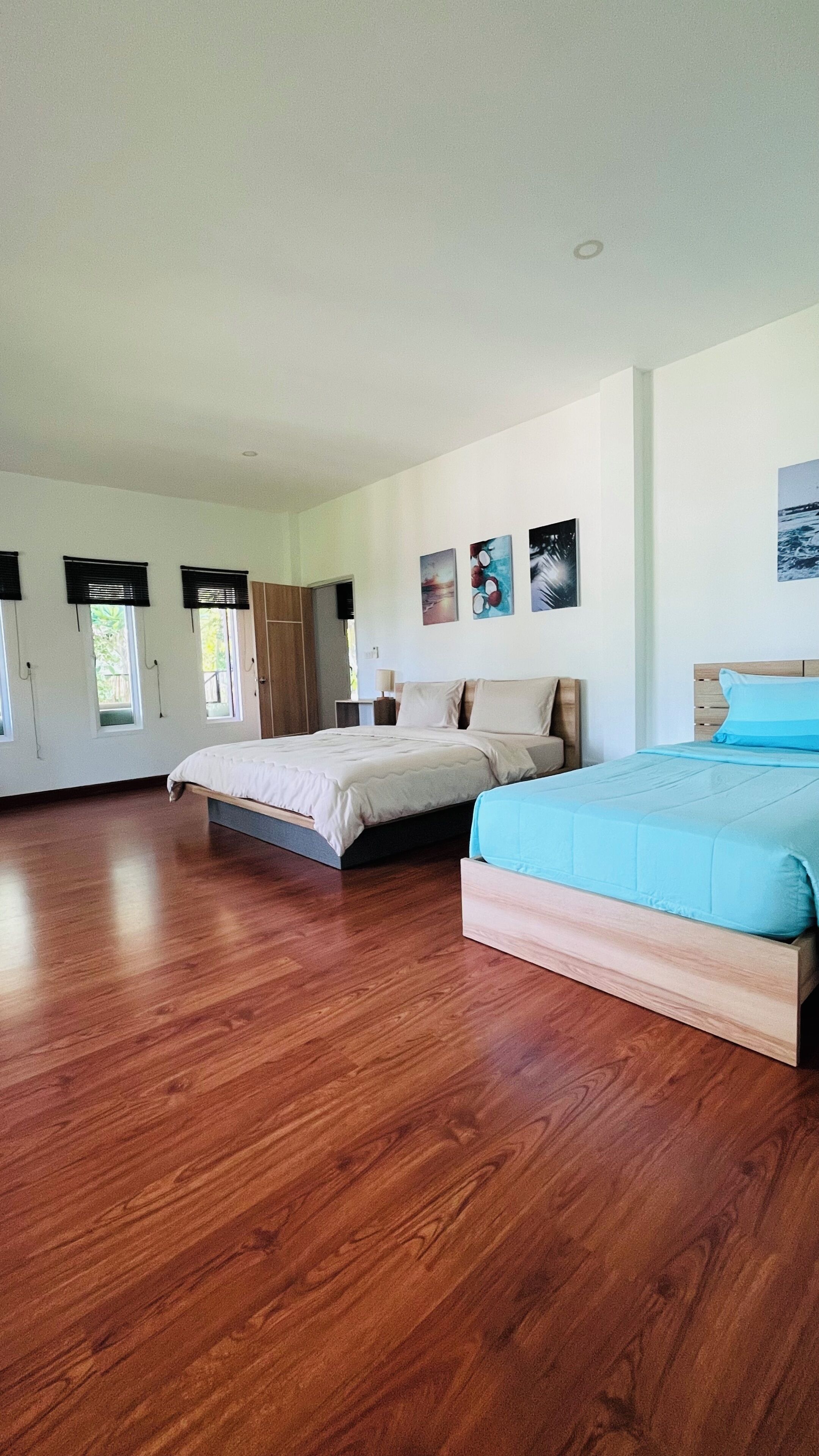 A spacious bedroom with two beds, wooden flooring, and a large window.