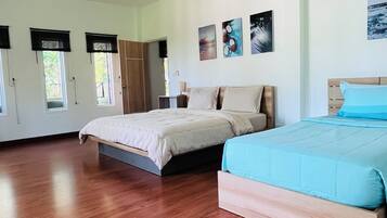 A spacious bedroom with two beds, wooden flooring, and a large window.