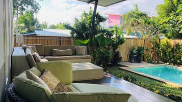Un espace extérieur aménagé, abrité et doté de meubles en osier, d’une piscine et d’une végétation luxuriante.