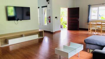 Un salon moderne doté d’un téléviseur à écran plat, de planchers en bois, d’une table basse en verre, d’un canapé et d’un coin repas avec des chaises.