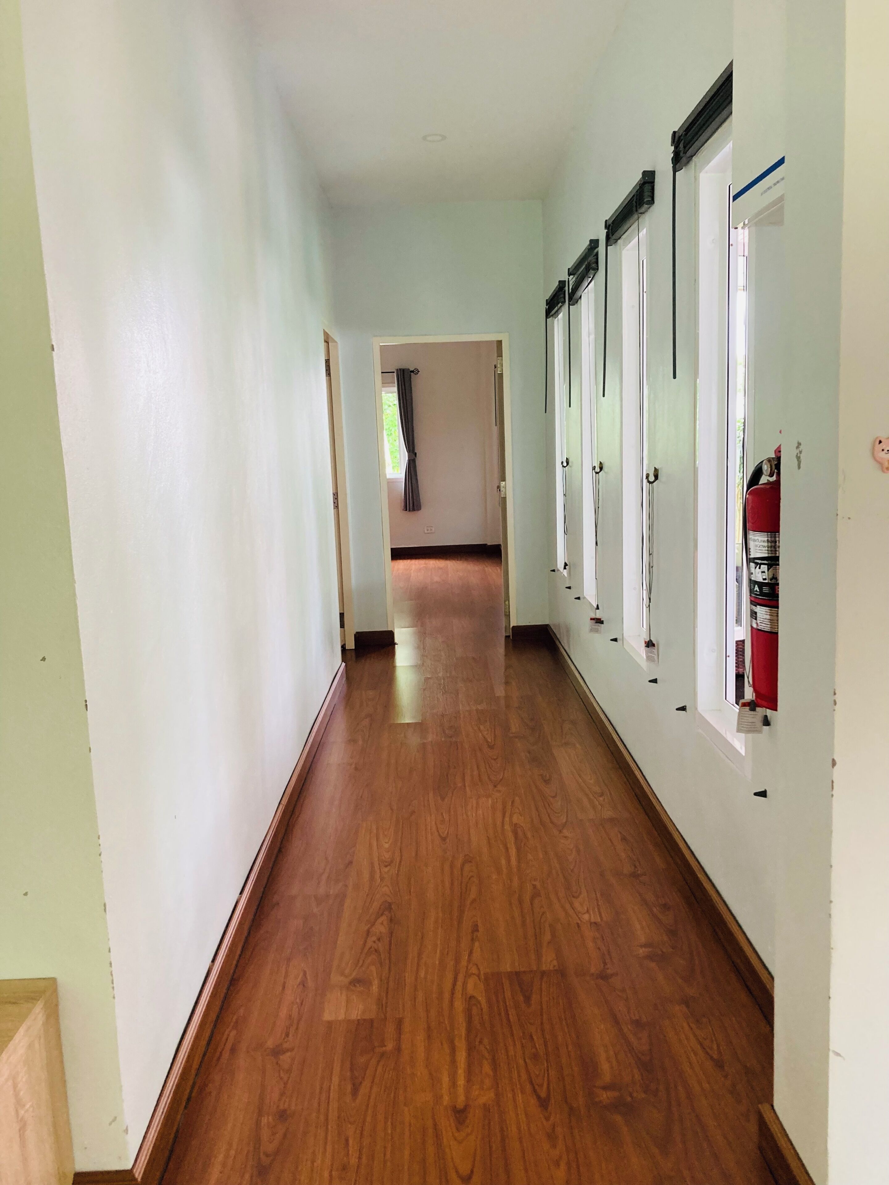 Un couloir doté d’un plancher en bois, de murs blancs et d’un extincteur fixé au mur.