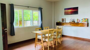 Un coin repas avec une table et des chaises en bois, une fenêtre avec des rideaux, une étagère remplie de jouets et un tableau accroché au mur.