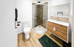 Et moderne badeværelse med en glasafskærmet brusekabine, et hvidt toilet, et træbord med vask og et spejl.