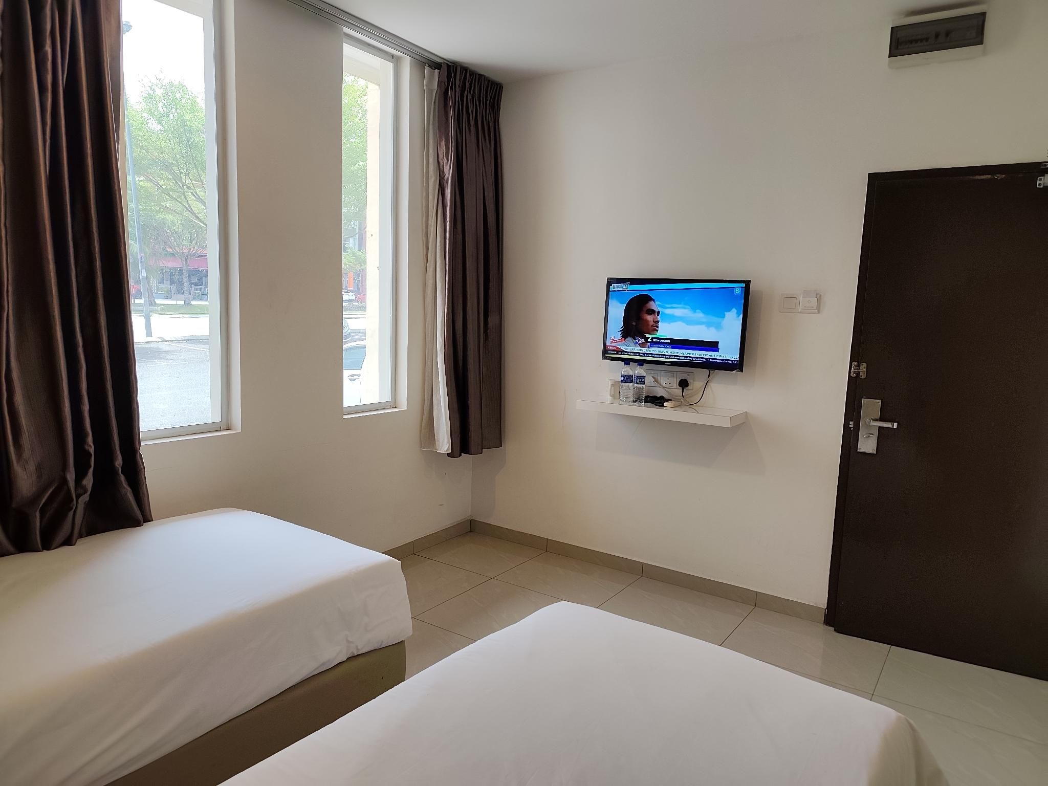 Una habitación de hotel con dos camas individuales, un televisor montado en la pared y una puerta.