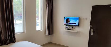 A hotel room with two single beds, a television mounted on the wall, and a door.