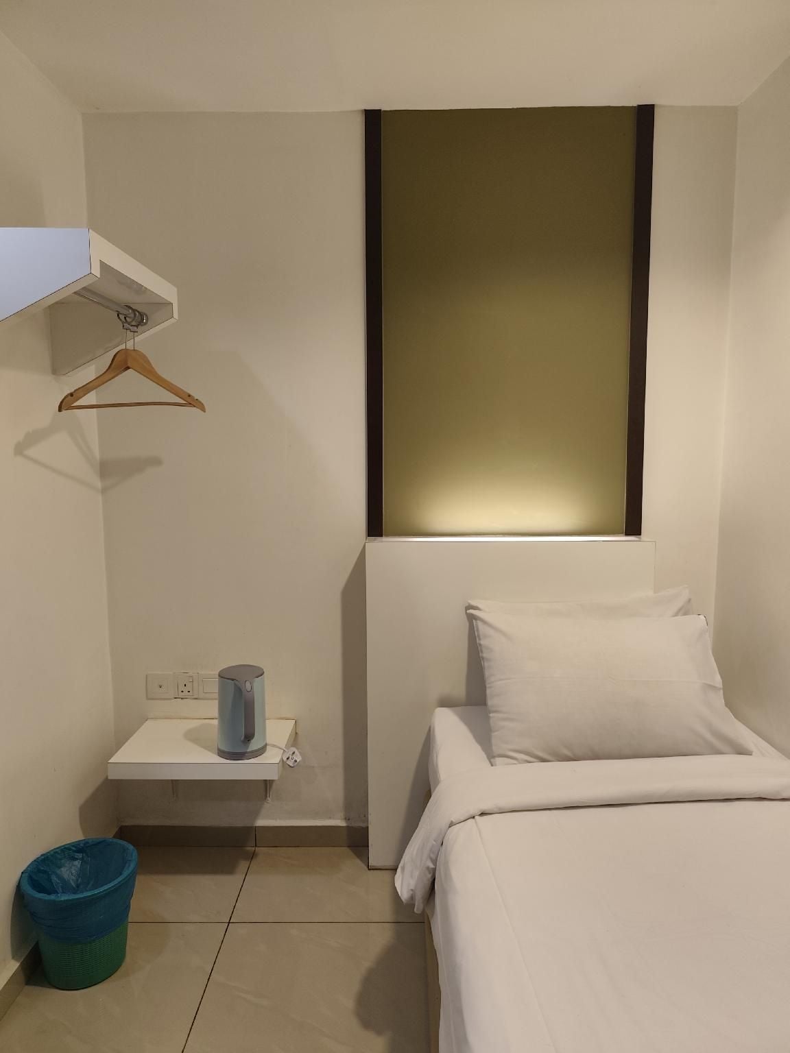 Habitación de hotel con cama, mesita de noche, un cubo de basura y estante en la pared.