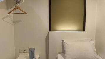 Habitación de hotel con cama, mesita de noche, un cubo de basura y estante en la pared.