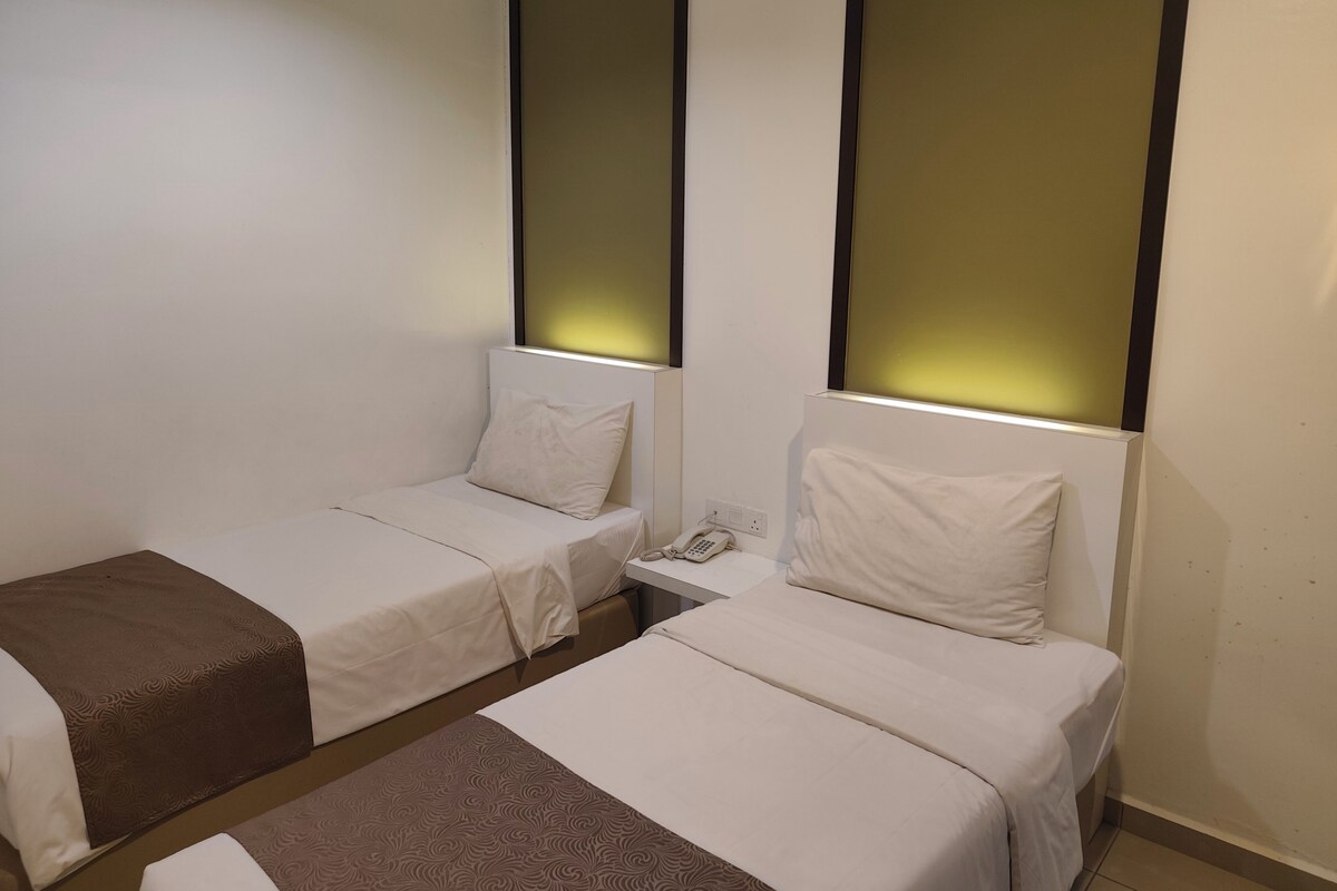 Een hotelkamer met twee enkele bedden, een nachtkastje met telefoon en een wandlamp.