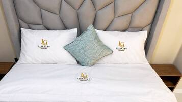 A bed with a geometric headboard, two pillows with a logo, and a decorative pillow.