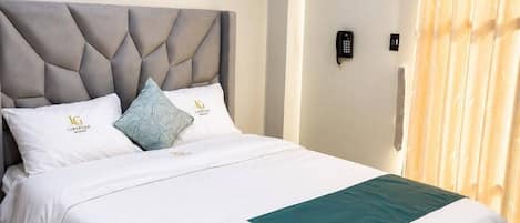 A hotel room with a bed, a painting, a telephone, and a curtain.