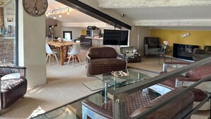 Ein großzügiger Wohnbereich mit Glastisch, Ledersofas, einem Fernseher und einem Essbereich mit Stühlen und Tisch.