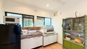 Una cocina con refrigerador, microondas, lavabo y un armario verde con vajilla.