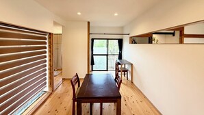 Una habitación con suelo de madera, una mesa de comedor con sillas, un ventanal con cortinas e iluminación empotrada en el techo.