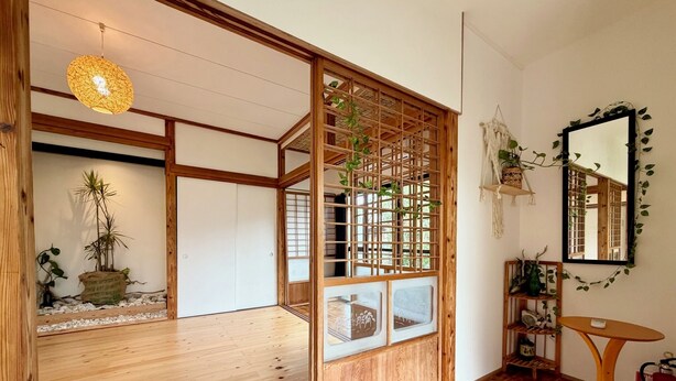 Una habitación japonesa tradicional con suelo de madera, un panel shoji, un aplique colgante y un espejo con plantas.