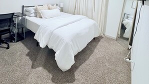 Hotellihuone, jossa on yksi sänky, työpöytä, tuoli, peili ja ilmanvaihtoaukko katossa.