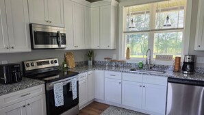 A kitchen with white cabinets, a stainless steel microwave, an oven, a coffee maker, and a window with blinds. - A Trip to the Nursery Capital (McMinnville)