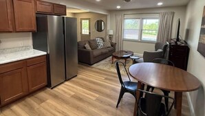 A compact kitchen with a refrigerator, wooden cabinets, and a dining area with a table and chairs. - The Reservoir House East (Andrews)