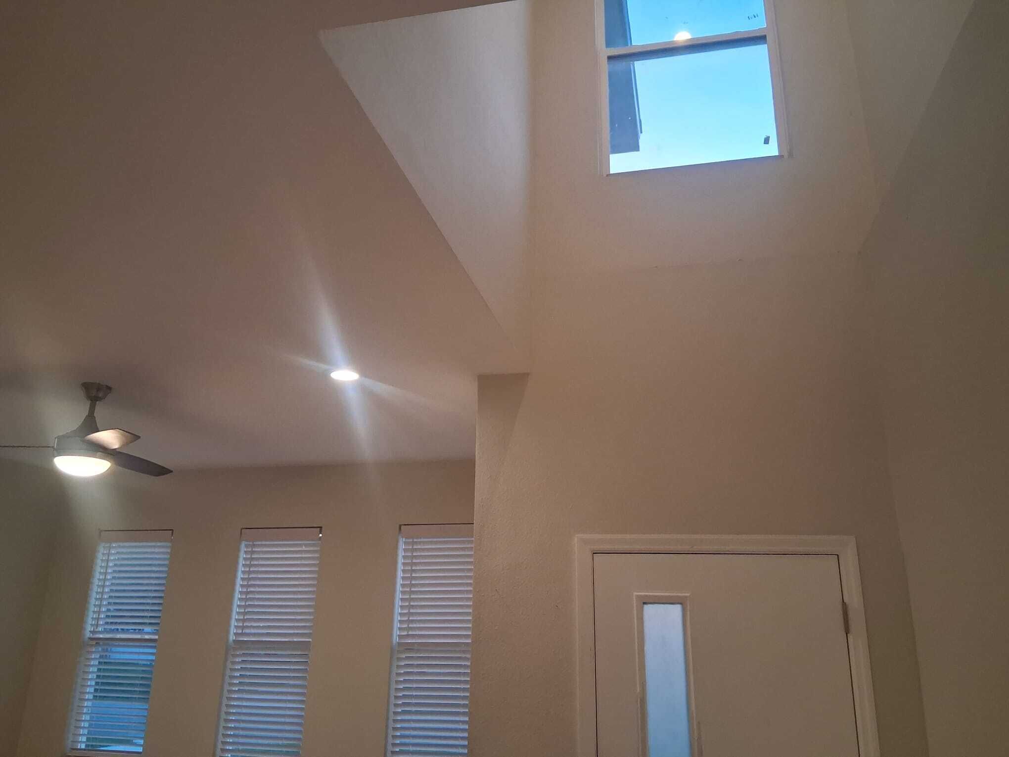 A room with a sloped ceiling, a ceiling fan, and three windows with blinds.