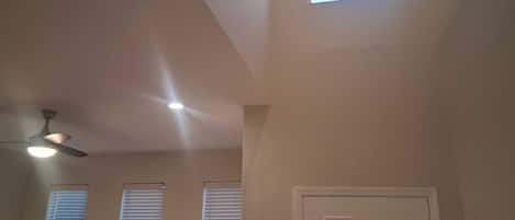 Une pièce avec un plafond en pente, un ventilateur de plafond et trois fenêtres équipées de stores.