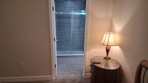 A bedroom with a bed, a nightstand with a lamp, a dresser, and a door leading to a shower area. - Serene 3-bedroom use in vibrant Orlando Close To Airport, Universal , Disney.... (Orlando)