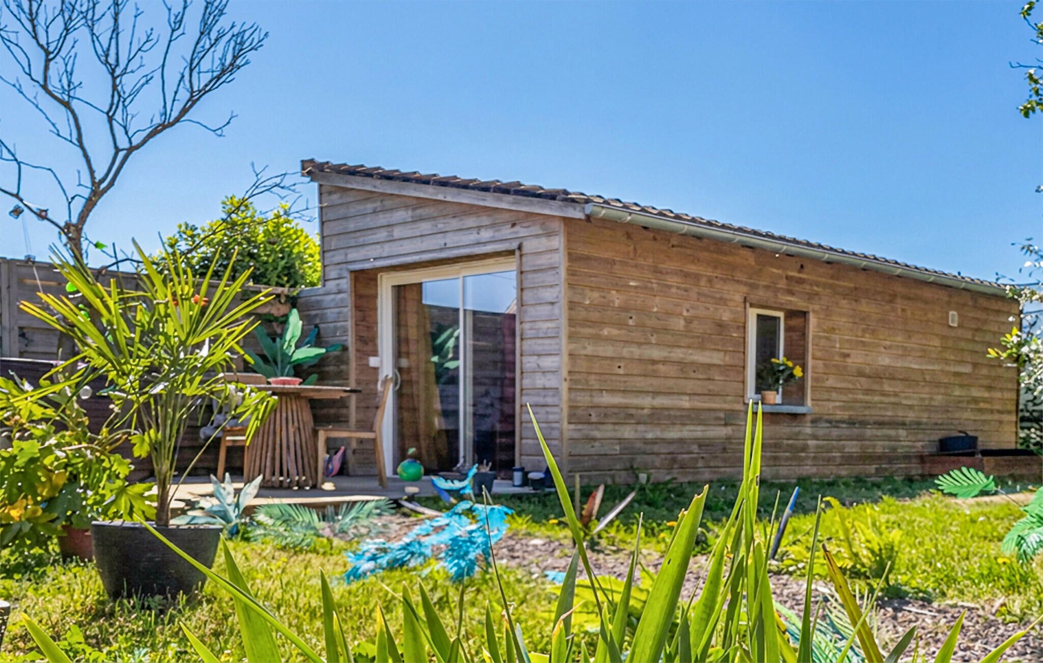 Eine Holzhütte mit einer Schiebetür, einem kleinen Fenster und einem Garten mit verschiedenen Pflanzen.