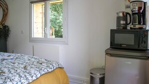 Een slaapkamer met een bed, een raam, een magnetron en een koffiezetapparaat.