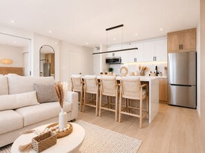 A modern kitchen with white cabinetry, a stainless steel refrigerator, and a dining area with a white table and chairs. - 32F Luxury Waikiki Ocean Suite w/ Parking (Honolulu)