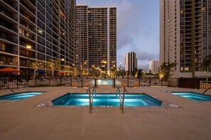 A hotel pool area with multiple swimming pools, surrounded by tall buildings and a clear sky. - 32F Luxury Waikiki Ocean Suite w/ Parking (Honolulu)