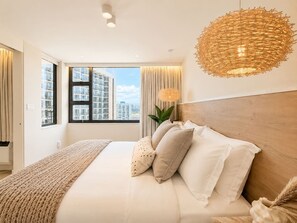 A modern hotel room with a large bed, a view of the cityscape, and a unique woven light fixture. - 32F Luxury Waikiki Ocean Suite w/ Parking (Honolulu)