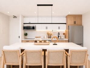 A modern kitchen with white cabinets, a stainless steel refrigerator, and a central island with a white countertop. - 32F Luxury Waikiki Ocean Suite w/ Parking (Honolulu)