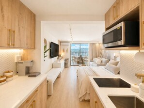 Une chambre d’hôtel moderne dotée d’une kitchenette, d’un grand lit, d’un canapé et d’un balcon offrant une vue sur la ville.