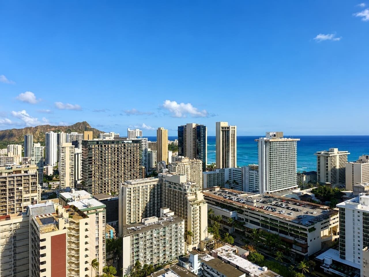 A cityscape with high-rise buildings, a parking lot, and a clear blue sky.