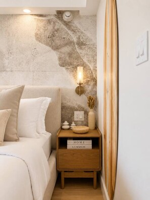 Ein Schlafzimmer mit Bett, Nachttisch, Wandlampe und einem kleinen Holznachttisch mit einem Schild.