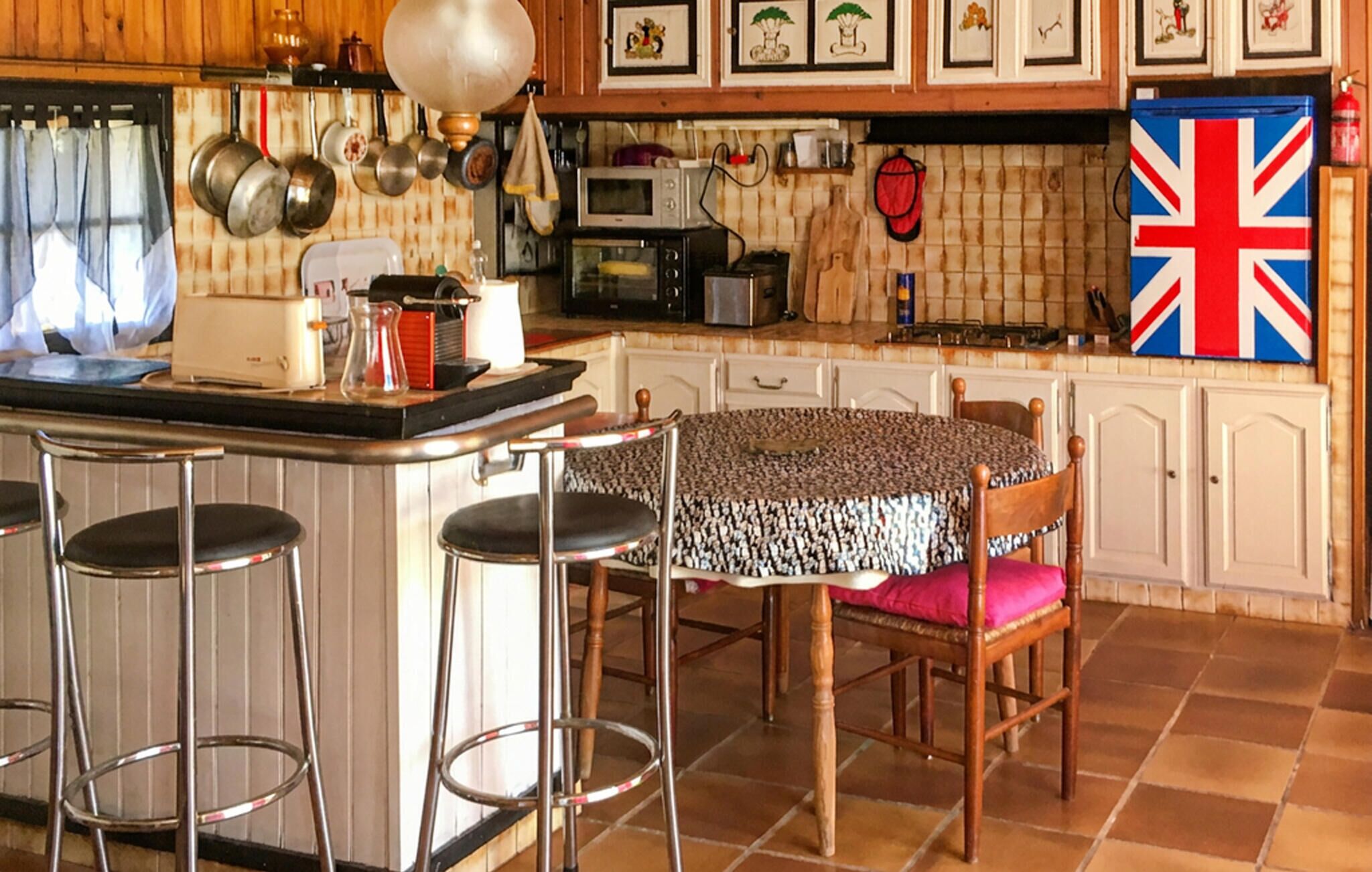 A kitchen with a bar area, stools, a table with chairs, and a Union Jack flag.