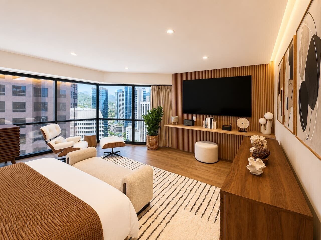 A modern hotel room with a large bed, a seating area, a TV, and a city view.