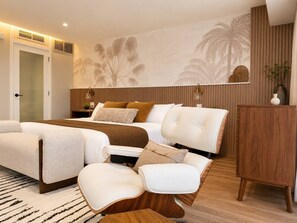 Ein modernes Schlafzimmer mit einem Bett, zwei weißen Sofas, einer Holzkassette und einer Wand mit Palmenmotiven.