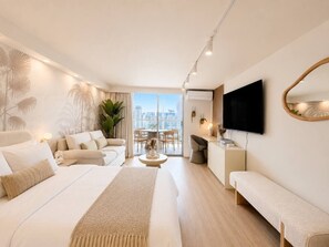 Habitació d'hotel moderna amb un llit gran, un sofà, una televisió i un balcó amb vista a la ciutat.