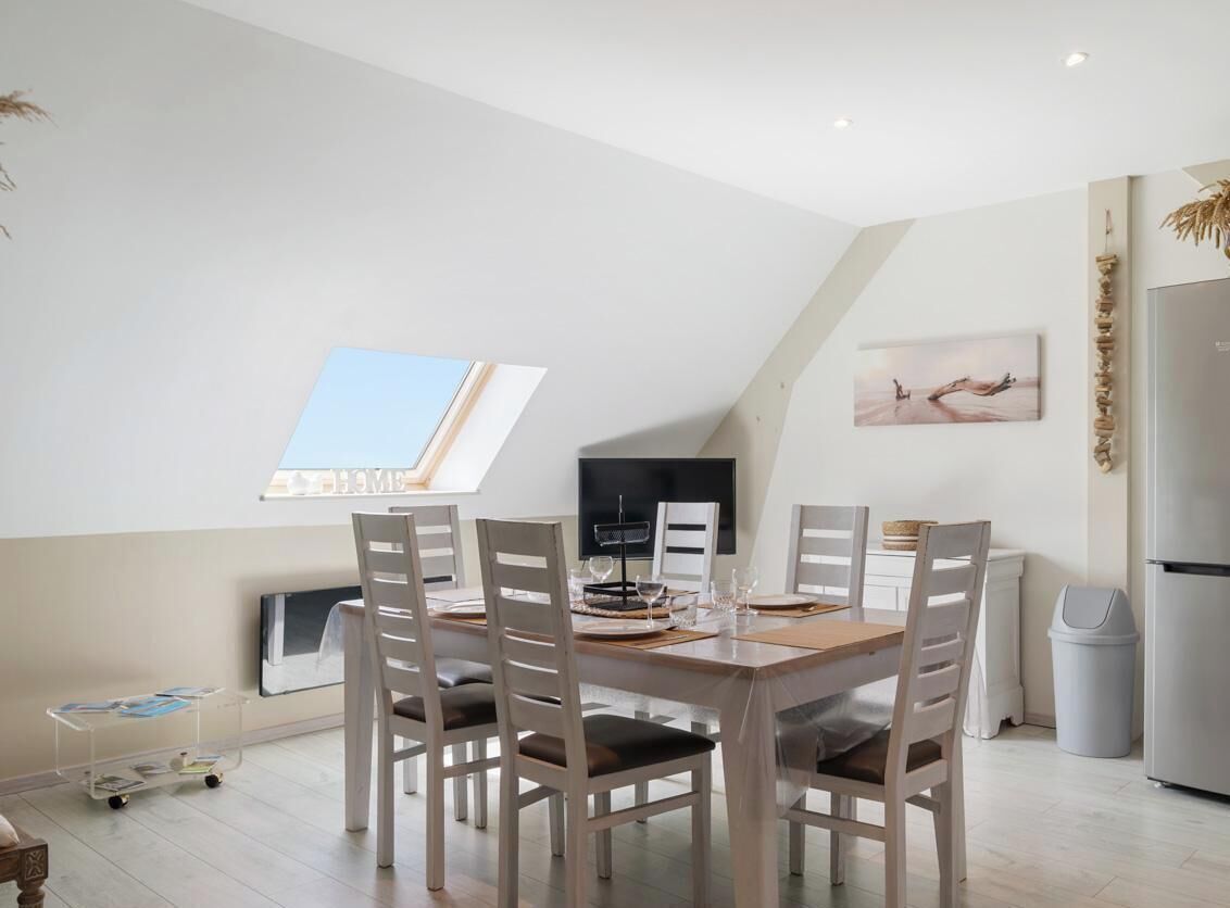 A dining area with a high ceiling, a table set for four, and a view of the sky through a skylight.