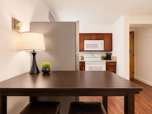 A kitchen with a dark wooden table, a lamp, a small plant, a microwave, and a white refrigerator. - Honolulu City Oasis 2BR with Free Parking (Honolulu)