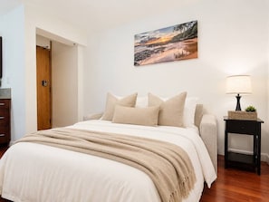 A bedroom with a bed, pillows, a blanket, a nightstand with a lamp, and a painting on the wall. - Honolulu City Oasis 2BR with Free Parking (Honolulu)
