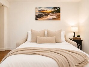 A bedroom with a bed, pillows, a blanket, a nightstand with a lamp, and a wall-mounted painting. - Honolulu City Oasis 2BR with Free Parking (Honolulu)