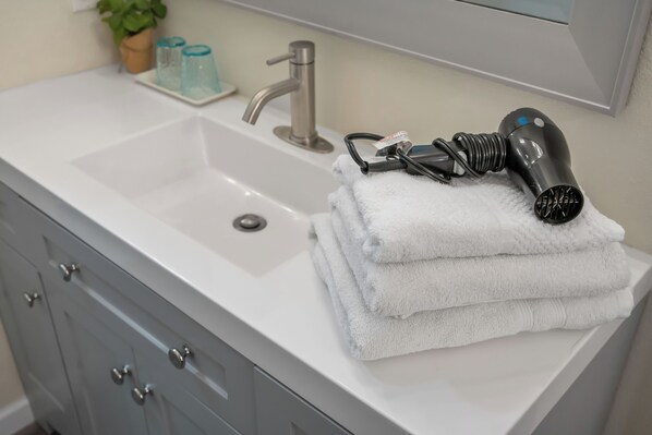 A bathroom with a white sink, a mirror, and a hairdryer on the counter.