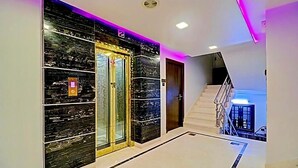 Un pasillo moderno con pared de mármol, un ascensor de vidrio y una escalera que conduce a un nivel superior.