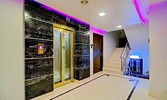 Un pasillo moderno con pared de mármol, un ascensor de vidrio y una escalera que conduce a un nivel superior.