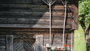 Un rustico chalet in legno con una porta a motivi a spina di pesce, un piccolo portico con un vaso di fiori e corna di cervo appese al muro.