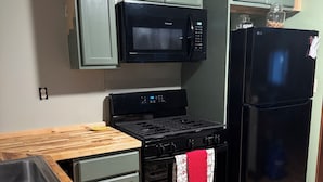 Eine Küche mit Mikrowelle, Herd, Kühlschrank und einer Holzausziehtafel.