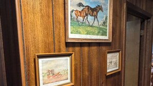 Eine Holzwand mit gerahmten Bildern von Pferden und einer Szene mit Menschen und einer Kutsche.